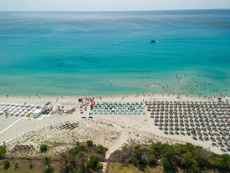 Vue aérienne d'une plage de sable fin bordée d'une mer turquoise et de parasols.
