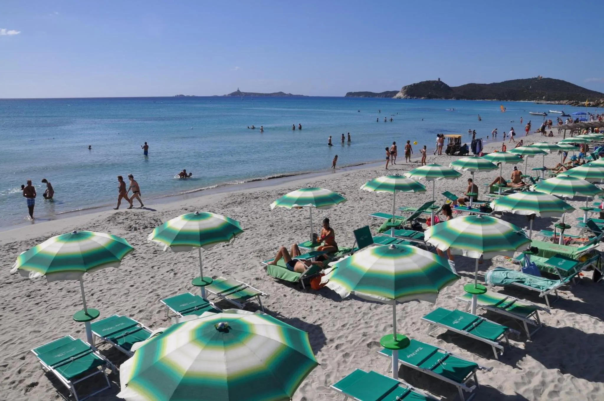 Plage de sable fin avec parasols rayés et transats alignés face à la mer.