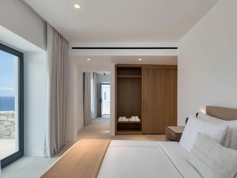 Chambre lumineuse avec un grand lit et un espace rangement ouvert.