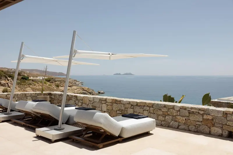 Transats blancs sous des parasols sur une terrasse surplombant la mer.