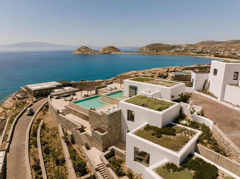Vue aérienne d'un complexe hôtelier blanc avec piscine à débordement et végétation luxuriante.