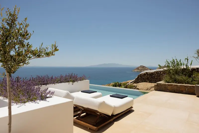 Deux transats blancs invitent à la détente au bord d'une piscine à débordement avec vue sur la mer.