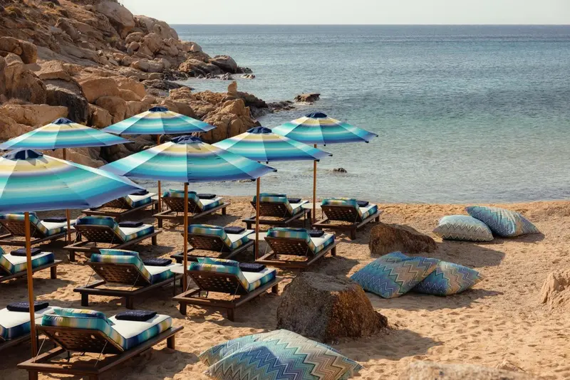 Transats colorés sous des parasols sur une plage de sable fin.