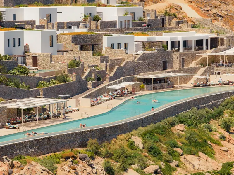 Vue aérienne d'un complexe hôtelier blanc avec piscine sinueuse et terrasses ensoleillées.