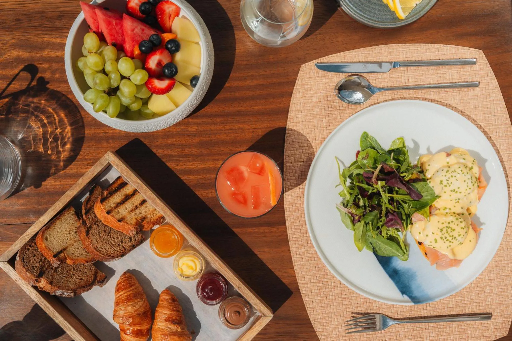 Une table en bois présente un petit-déjeuner avec des fruits, des viennoiseries et des boissons.