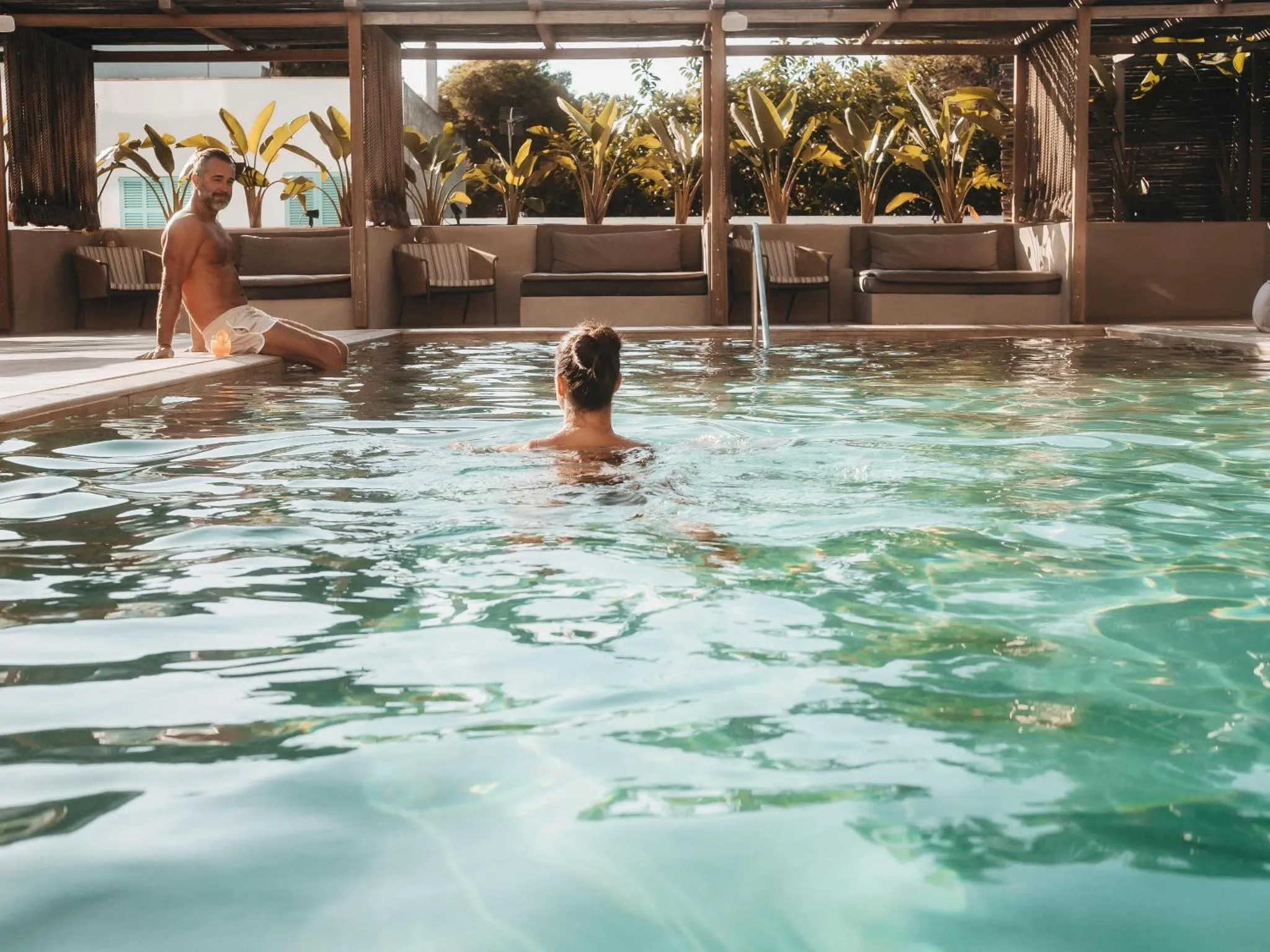 Deux personnes se détendent au bord d'une piscine ensoleillée.
