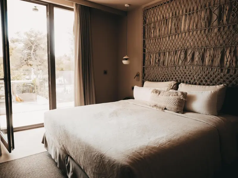 Une chambre lumineuse avec un grand lit et une décoration murale en macramé.