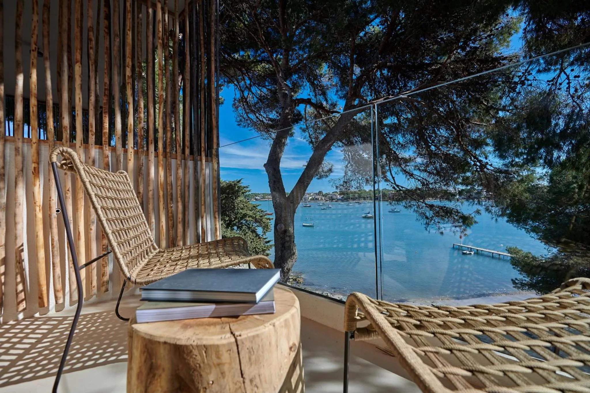 Deux fauteuils en osier invitent à la détente sur une terrasse en bois avec vue sur la mer.