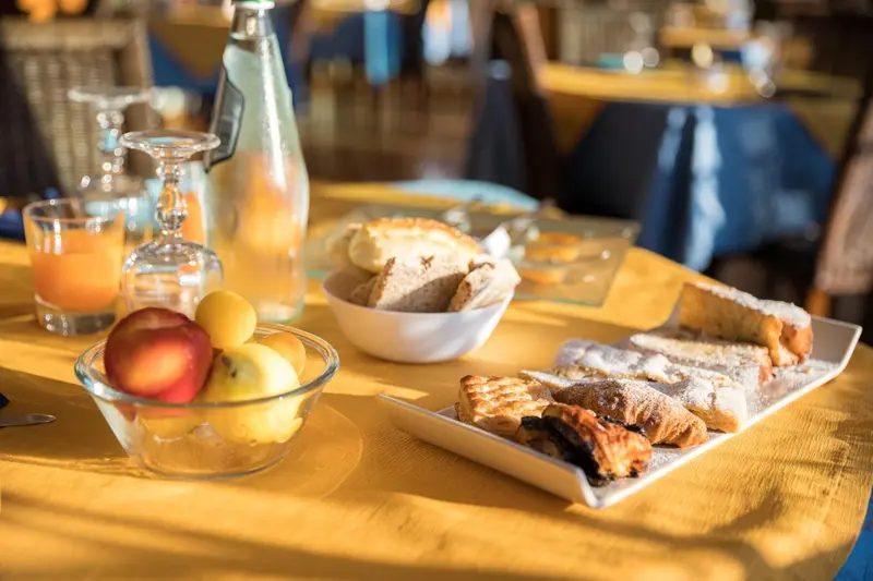 Une table jaune est dressée avec des viennoiseries, des fruits et des jus.