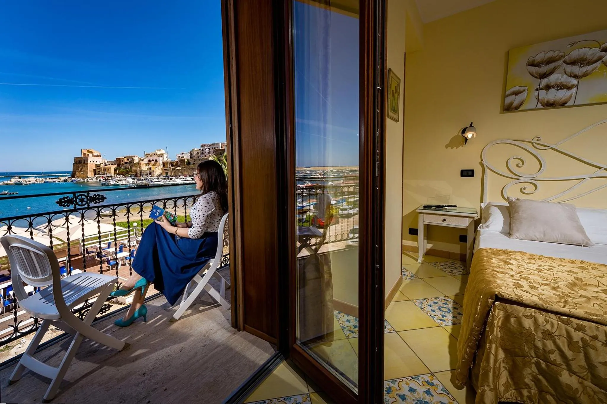 Une femme assise sur une terrasse ensoleillée regarde la mer.