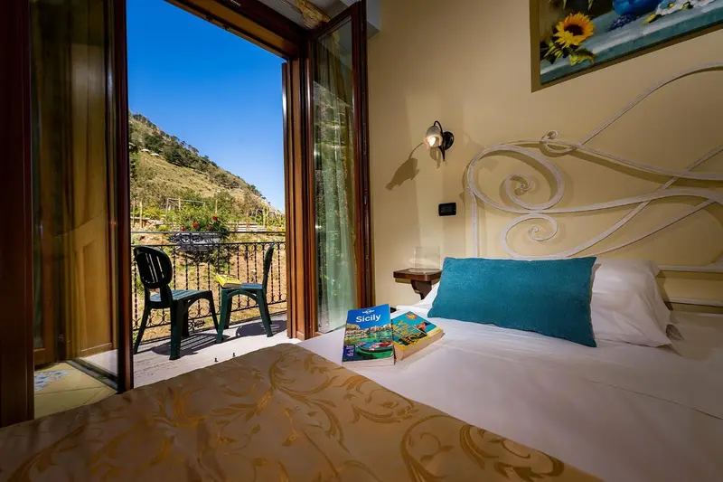 Une chambre lumineuse s'ouvre sur un balcon avec vue sur les collines.