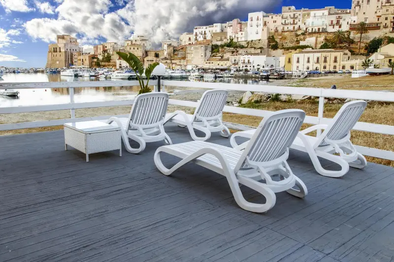 Terrasse avec chaises longues face à un port de plaisance et une ville côtière.
