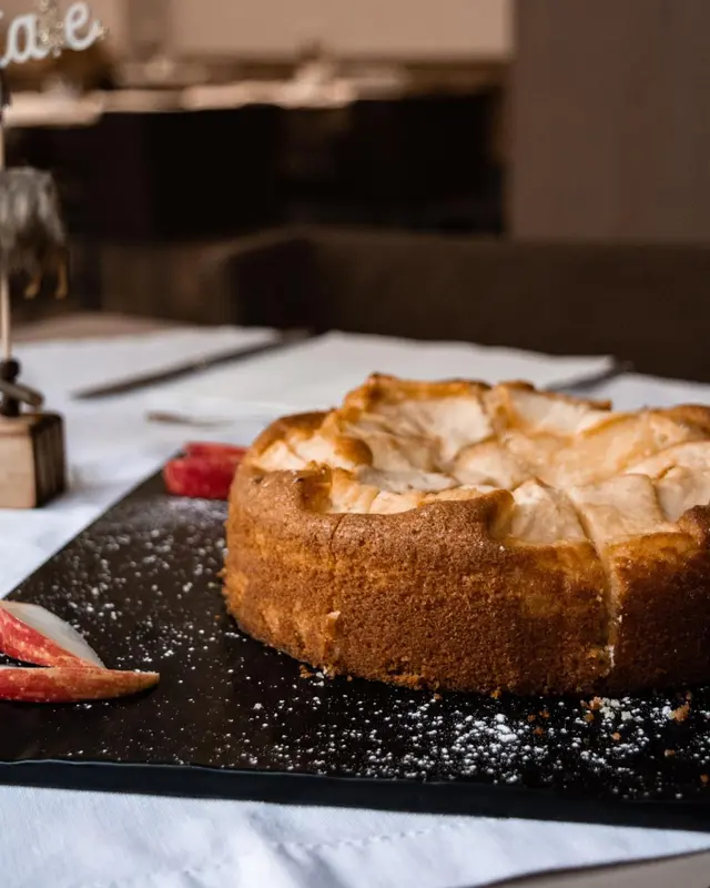 Un gâteau aux pommes est présenté sur une planche sombre.