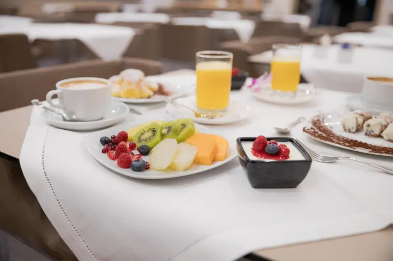 Une table est dressée avec un petit-déjeuner composé de fruits frais, de viennoiseries et de boissons.
