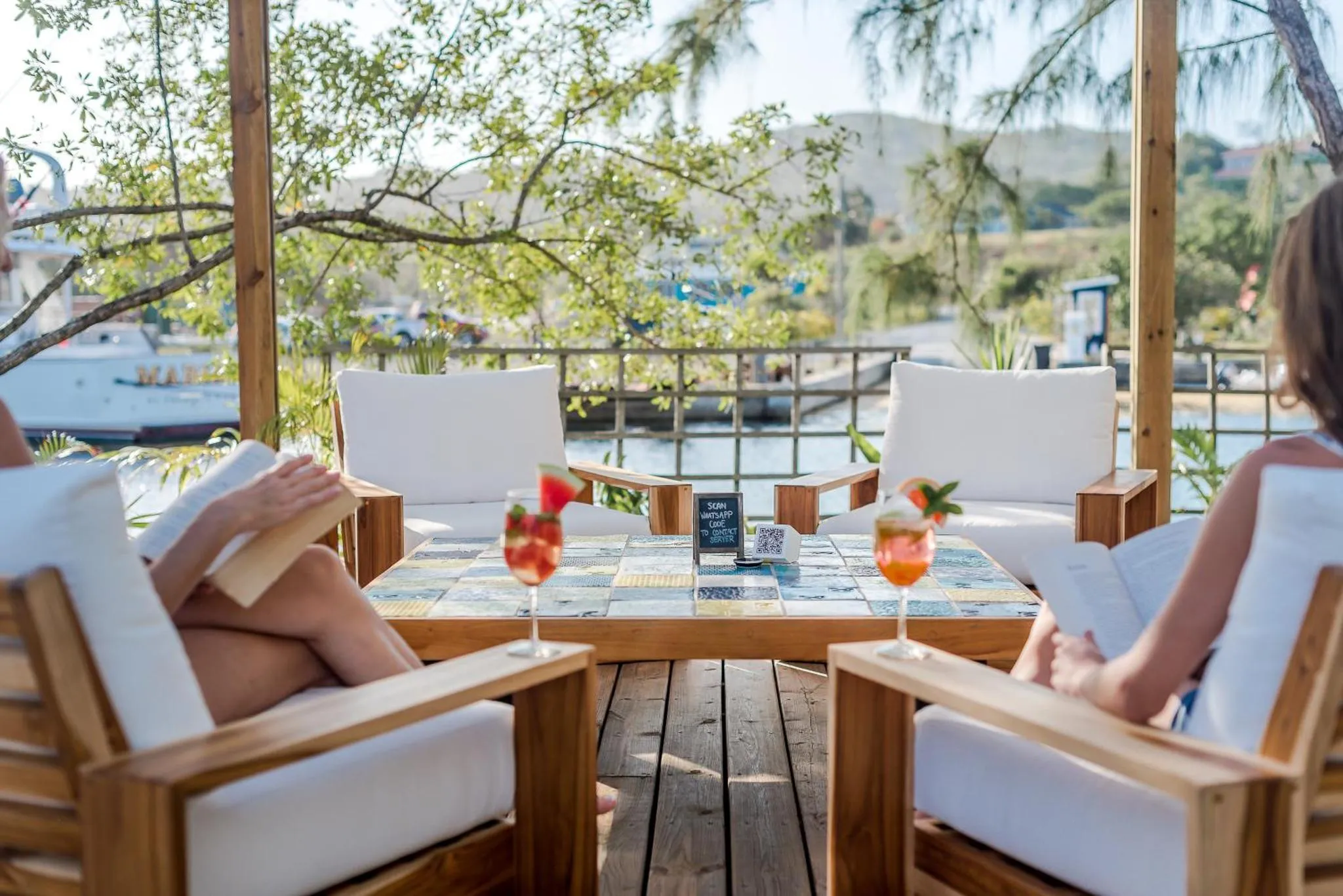 Deux personnes assises à une table en bois avec des boissons colorées sur une terrasse ensoleillée.
