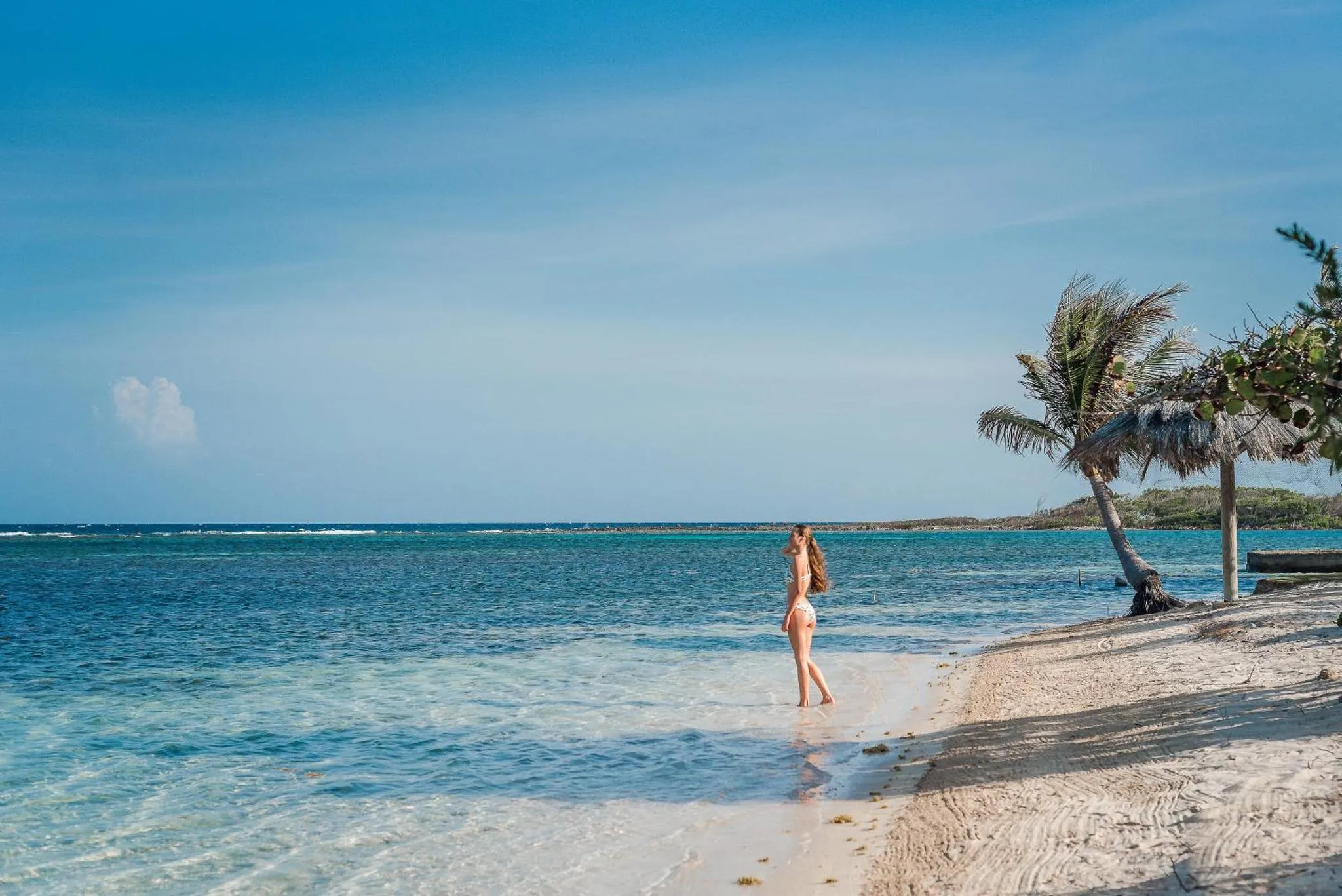 Une personne se tient sur une plage de sable blanc face à la mer turquoise.