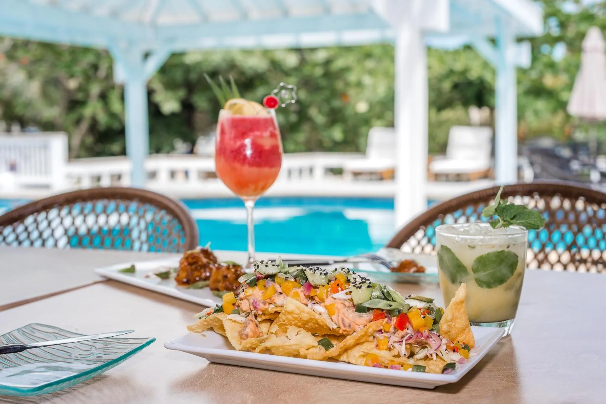 Des plats et des boissons colorées sont servis sur une table près d'une piscine.