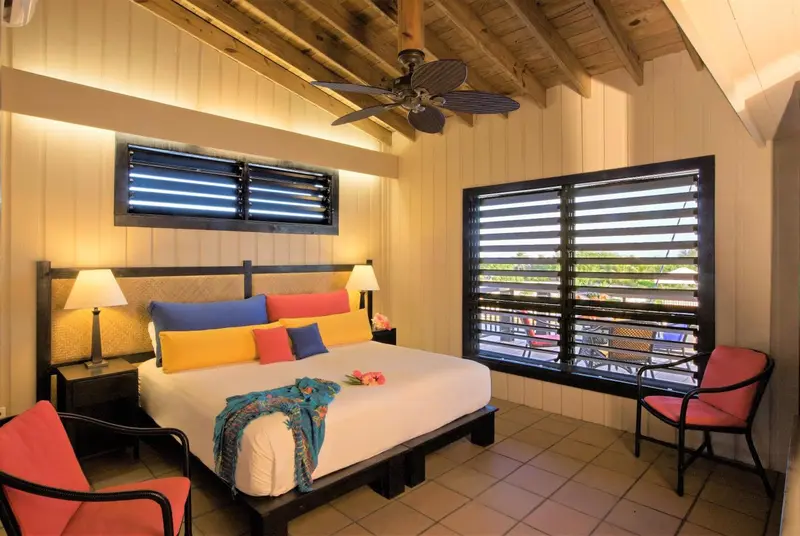 Une chambre lumineuse avec un lit recouvert d'oreillers colorés et deux fauteuils.