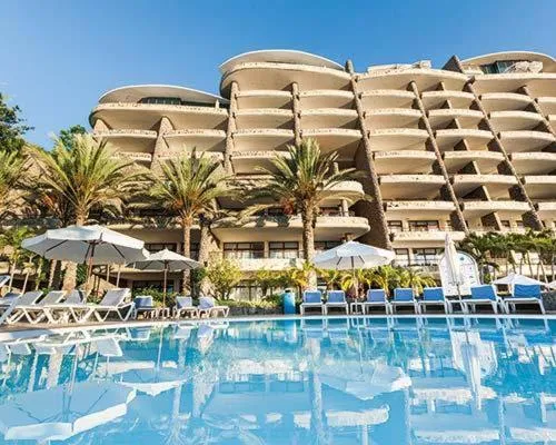 Vue d'une piscine devant un bâtiment aux terrasses ensoleillées.