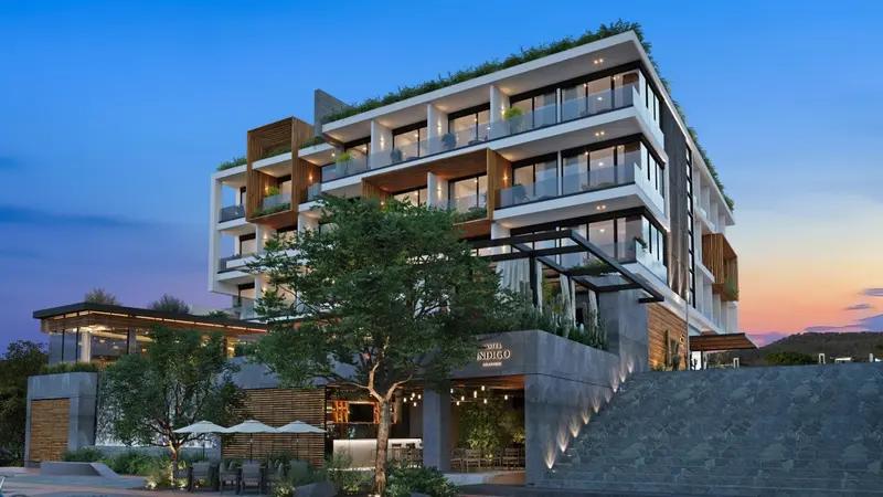 Bâtiment moderne avec des balcons et une végétation luxuriante au coucher du soleil.