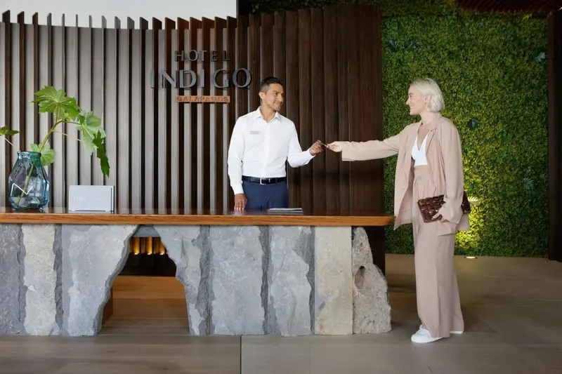 Un employé d'hôtel accueille une cliente à la réception.
