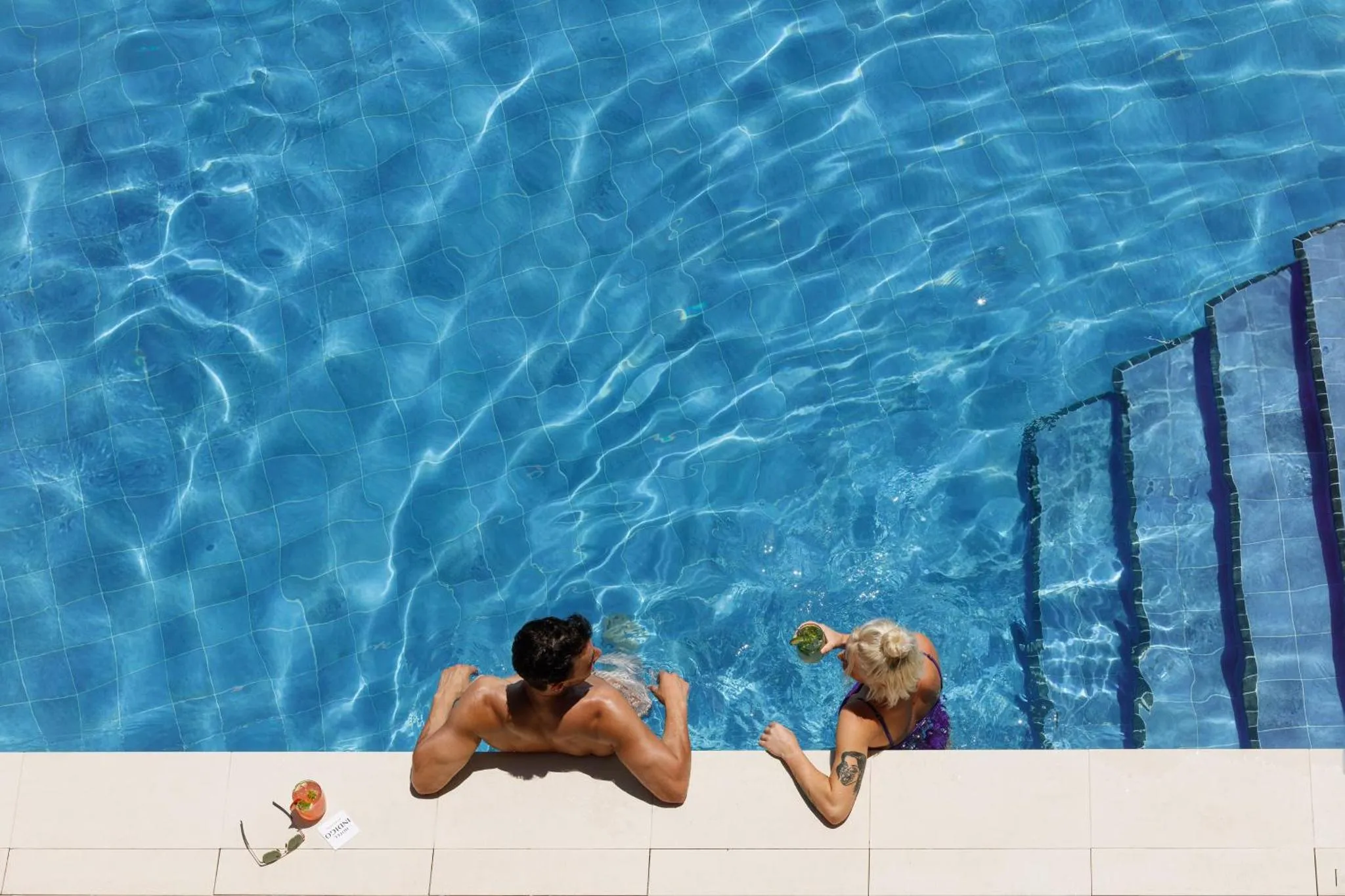 Deux personnes se détendent au bord d'une piscine ensoleillée.