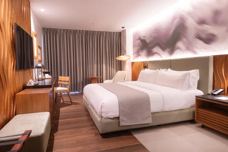 Une chambre lumineuse avec un grand lit et un décor mural abstrait.