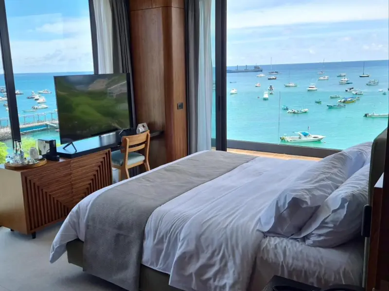 Une chambre avec un grand lit face à une baie vitrée donnant sur la mer.