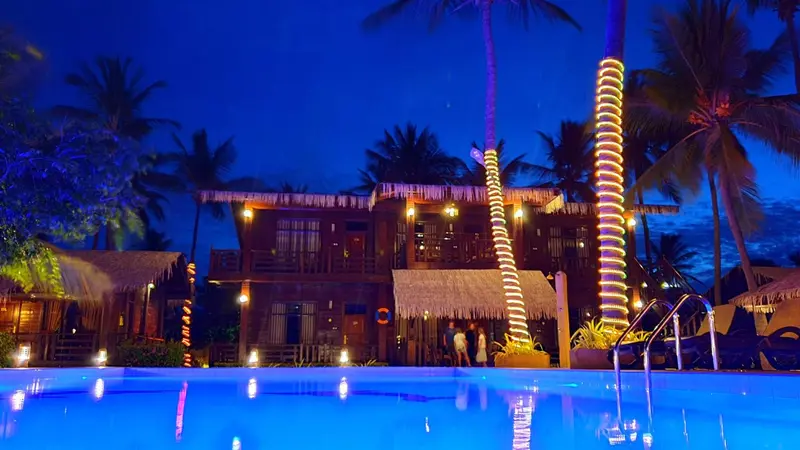 Bâtiment éclairé aux palmiers et piscine illuminée en soirée.