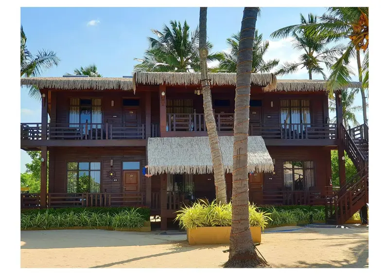 Bâtiment en bois sur pilotis avec plusieurs balcons et végétation tropicale.