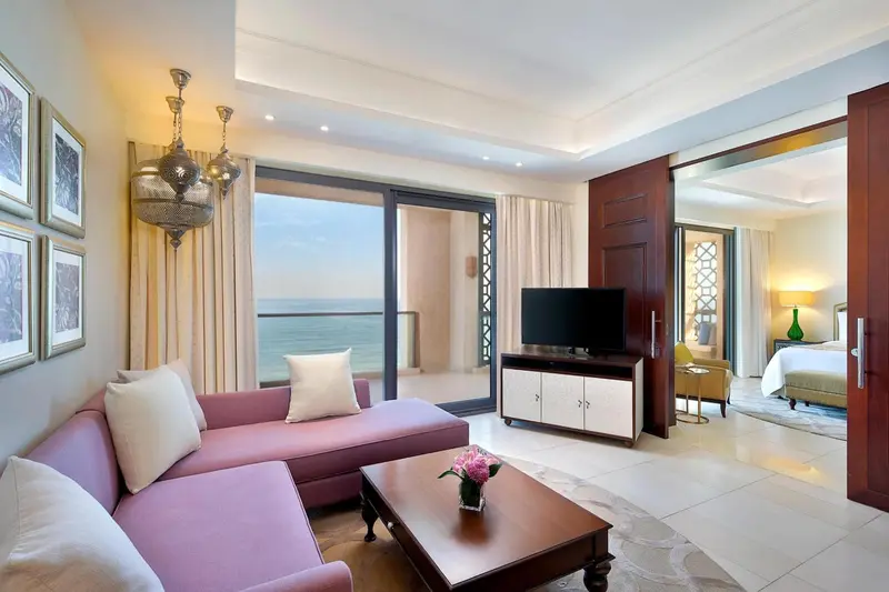 Un salon spacieux avec canapé rose et vue sur la mer par de grandes baies vitrées.