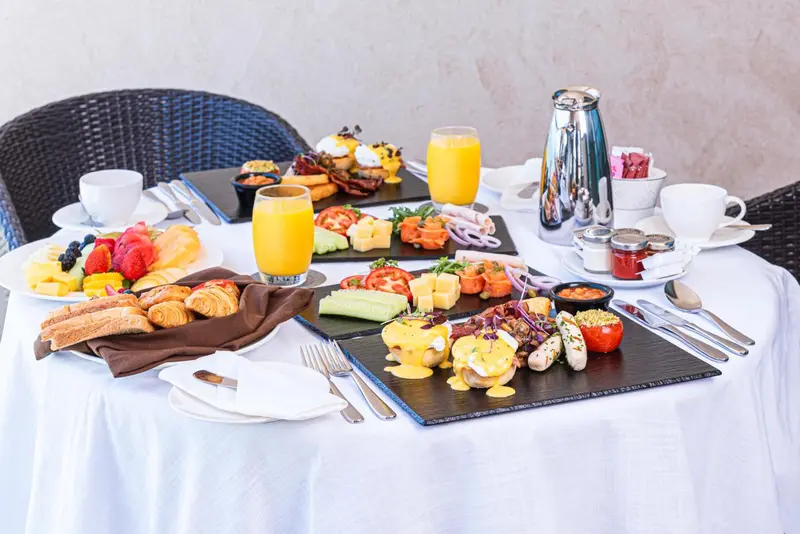 Table dressée pour un copieux petit-déjeuner avec viennoiseries, fruits et plats salés.