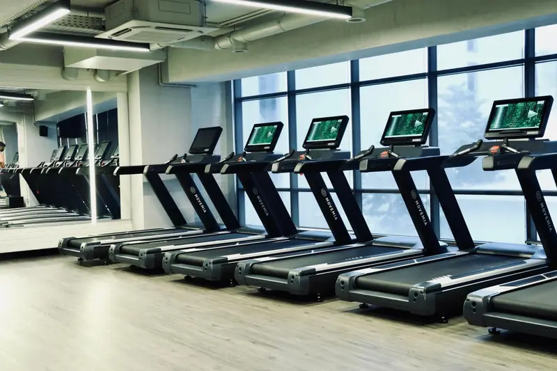 Une salle de sport lumineuse avec plusieurs tapis de course face à de grandes fenêtres.
