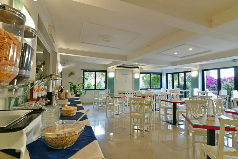 Une salle lumineuse avec un buffet propose des tables et des chaises pour les repas.