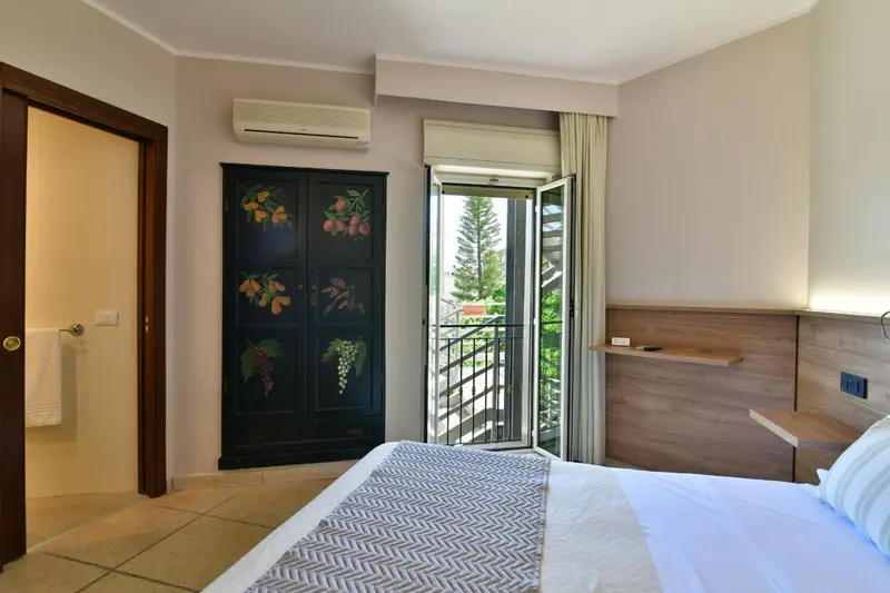 Une chambre lumineuse avec un lit fait et un balcon ouvert sur un jardin.