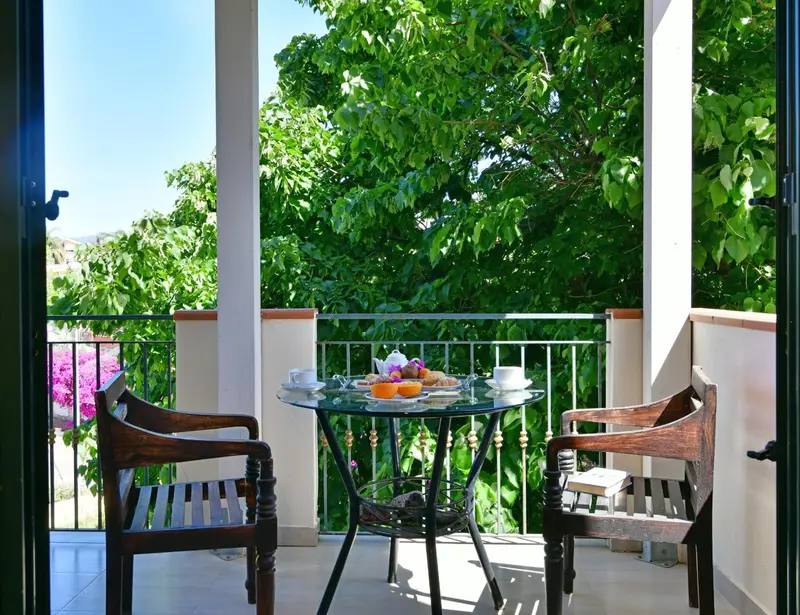 Une table ronde avec un petit-déjeuner est mise en scène sur une terrasse ombragée.