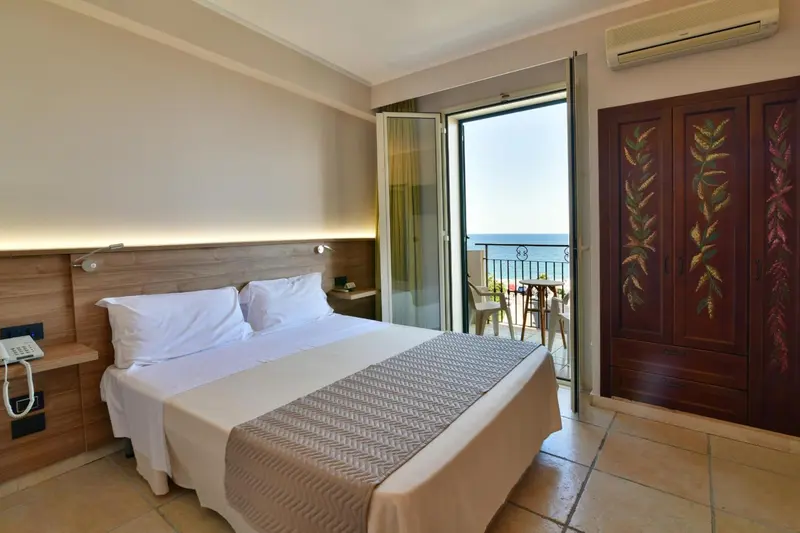 Une chambre lumineuse avec un lit double et un balcon donnant sur la mer.