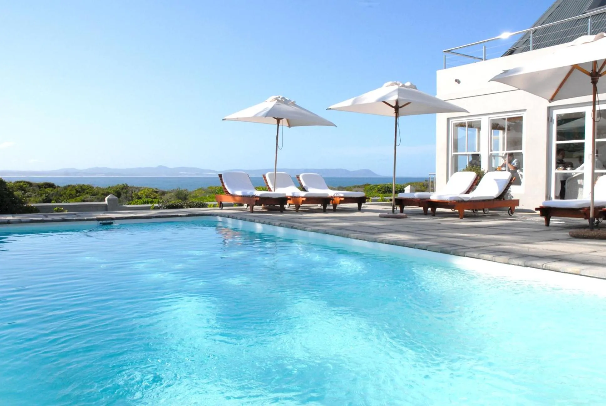 Transats blancs alignés au bord d'une piscine turquoise avec vue sur la mer.