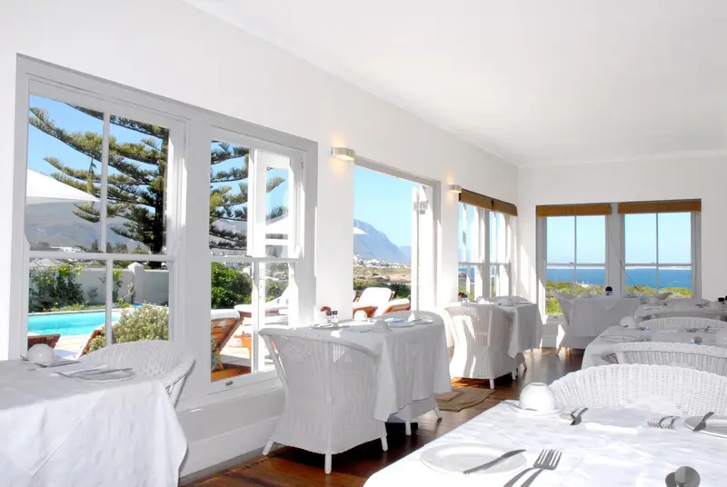 Une salle lumineuse avec des tables dressées face à une vue sur la mer.