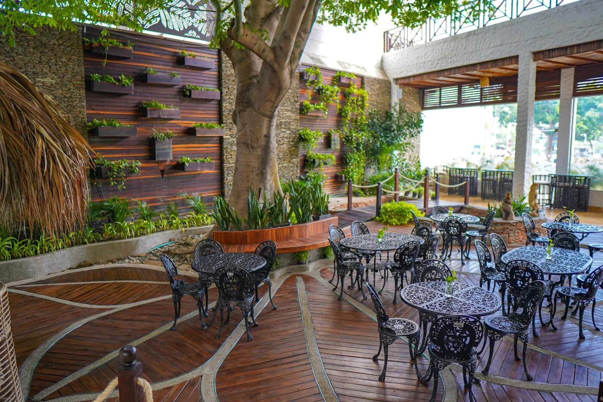 Terrasse ombragée avec tables et chaises en fer forgé, entourée de végétation luxuriante.