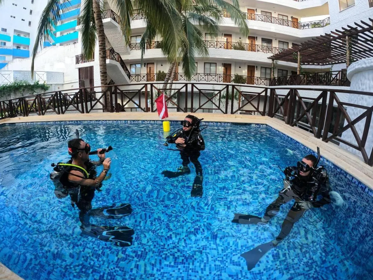 Trois personnes en équipement de plongée se tiennent dans une piscine turquoise.