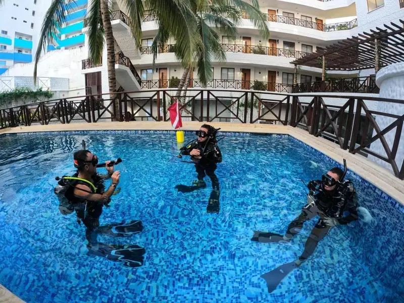 Trois personnes en équipement de plongée se tiennent dans une piscine turquoise.