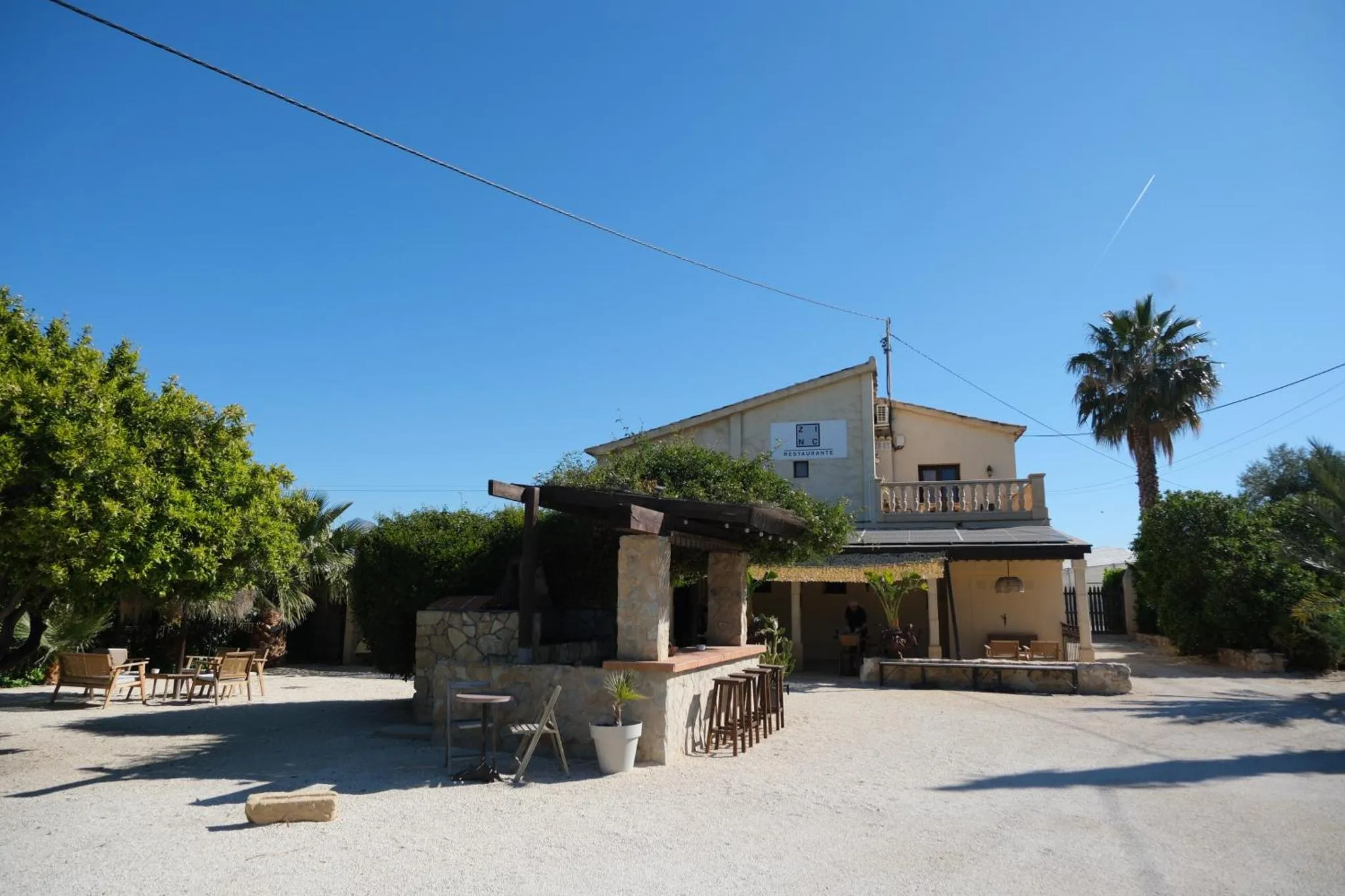 Bâtiment blanc avec une pergola ombragée et une cour gravillonnée ensoleillée.