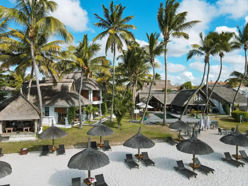 Vue aérienne d'un complexe hôtelier tropical avec des parasols et des chaises longues sur une plage de sable blanc.