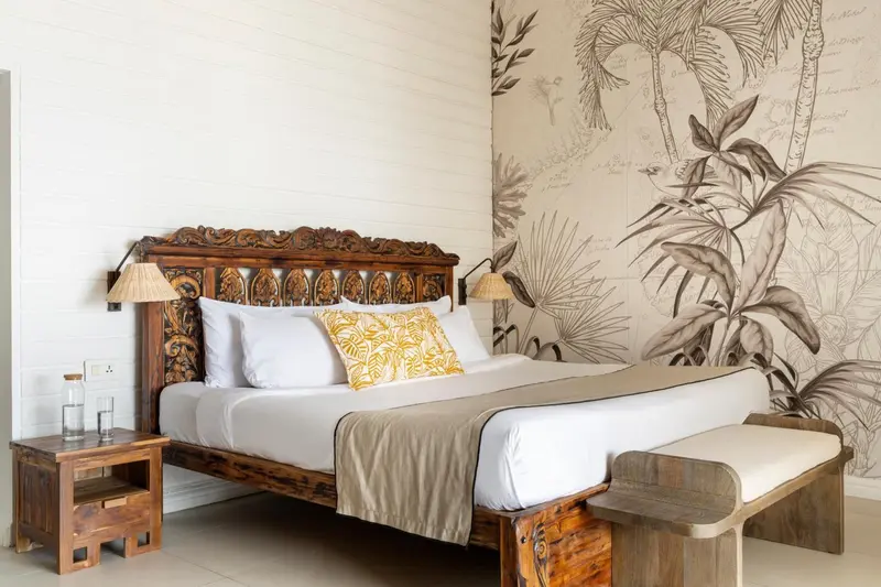 Une chambre lumineuse avec un grand lit en bois sculpté et un papier peint à motifs tropicaux.