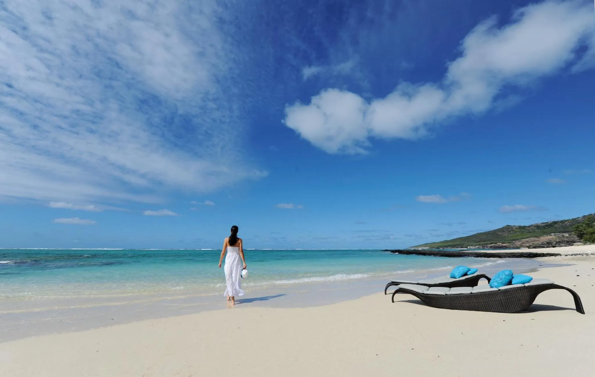 Une femme marche sur une plage de sable blanc face à la mer turquoise.