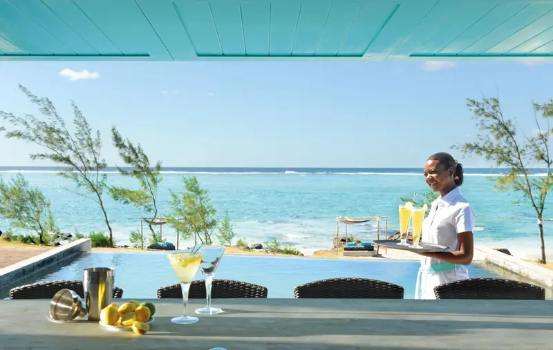 Une serveuse propose des cocktails devant un bar avec vue sur la mer.