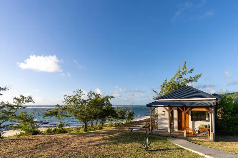 Un bungalow en bois avec une terrasse face à la mer et à la végétation.