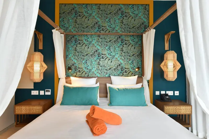 Lit double avec oreillers et coussins turquoise dans une chambre décorée de motifs végétaux.