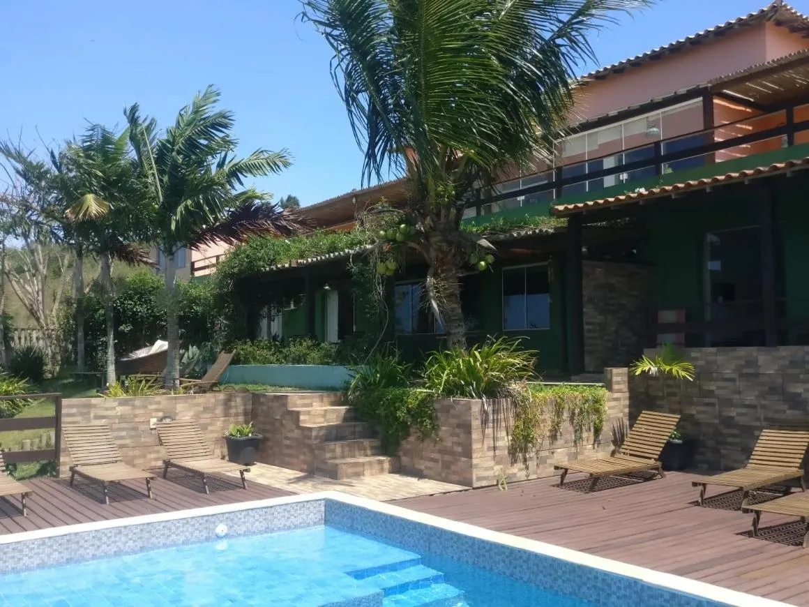 Bâtiment vert avec piscine et chaises longues devant un jardin tropical.